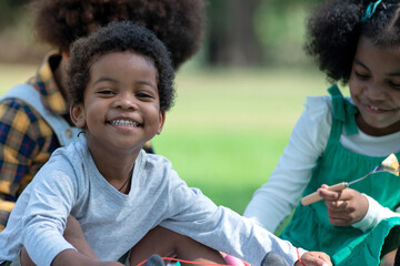 African little boy laughing happily sitting in group of friends in park