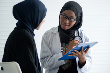 African Muslim doctor inquires about young Muslim woman patient about illness, both of them wore...