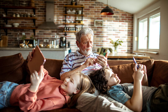 Grandfather and grandchildren using their gadgets together on the couch at home