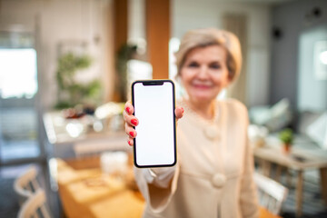 Senior woman showing the camera a smartphone with a blank screen at home