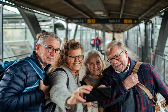 Group of senior friends taking selfies on a smartphone at the train station