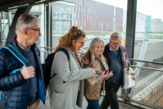 Group of senior friends checking for the arrival of their train on a smartphone in the station
