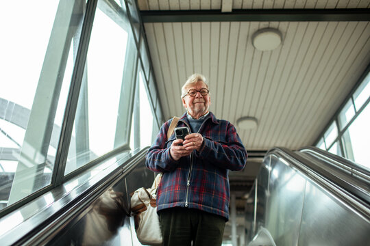 Senior man using his smartphone on a escalator at the train station - Powered by Adobe
