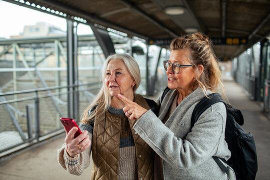 Two senior female friends looking for directions on a smartphone at the train station