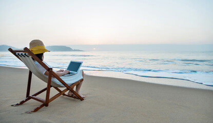 Woman sitting on beach and working with laptop.