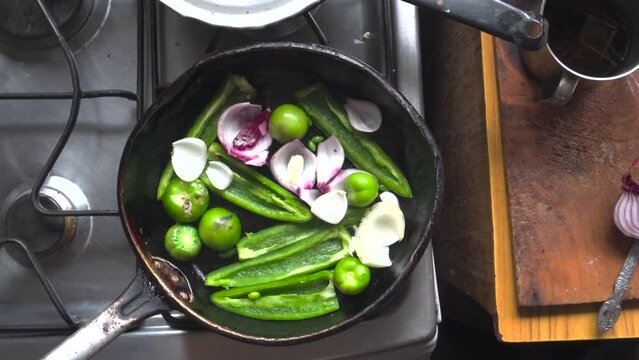 Acercamiento de Manos asando vegetales, mil tomate, chile pimiento, cebolla morada, en una sat&eacute;n r&uacute;stica en una cocina