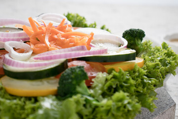 White wooden table with a handmade vegan salad with pieces of pieces of lettuce, broccoli, tomato, zucchini and carrot.