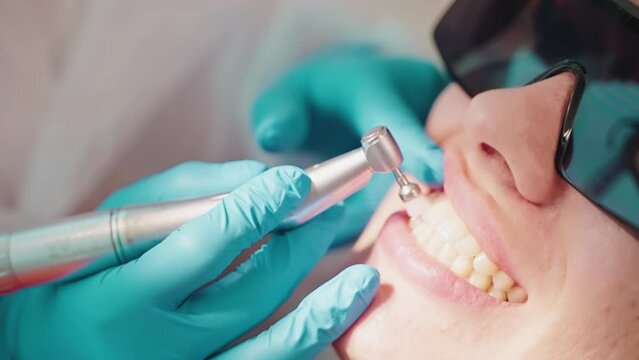Stomatologirst makes hygienic cleaning teeth in dentistry for woman.