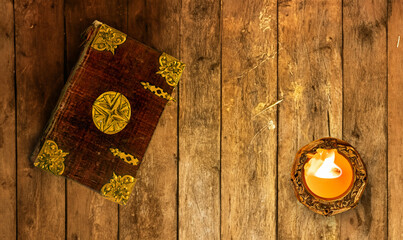 An old book with decorative cover with candle on an old table from planks