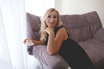 Middle aged woman posing at home. The mature model hold a cup of tea and drink