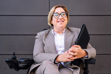 portrait of a smiling business woman using a electric wheelchair holding a folder looking at...