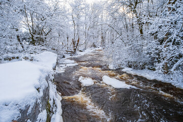 Fototapeta na wymiar Flowing river in a wintry landscape by a forest