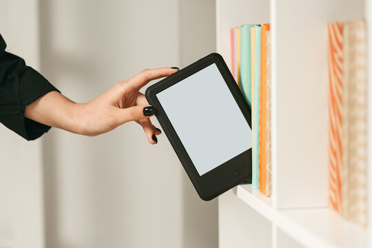 Man taking modern e-book reader from a bookshelf close up