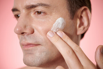 Middle-aged man applying anti-aging face cream in the morning