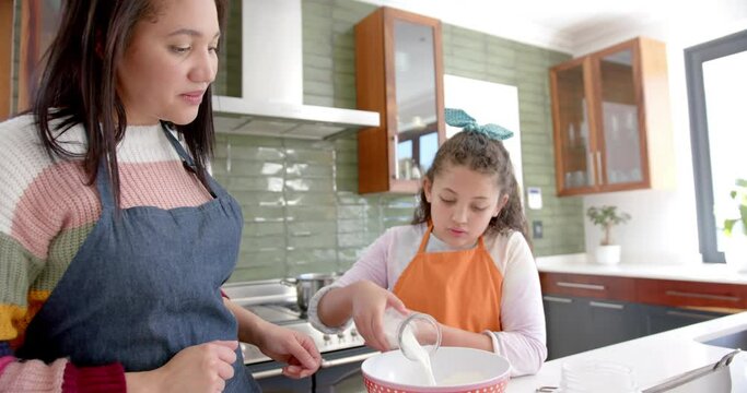 Happy biracial mother and daughter preparing dough and smiling in sunny kitchen