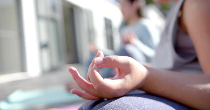 Happy biracial mother and daughter practising yoga on terrace in sunny day, slow motion