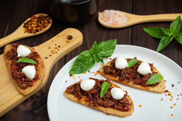 Caprese toasts with mini mozzarella cheese, dry tomatoes and basil. Traditional Calabrian food. Antipasti