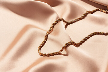 Golden chain necklace on silk background close up