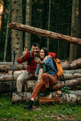 Two hikers find a peaceful spot on a log amidst the wilderness, using technology to bring their mountain adventure to life through a video call.