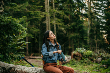 A peaceful Latin woman takes a pause on a tree log during her mountain trek, finding solace in the...