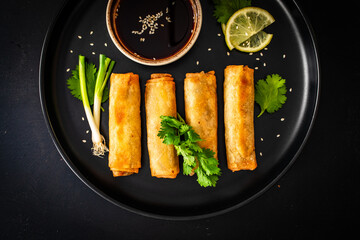 Vegetable filled spring rolls and soy sauce on black wooden table 