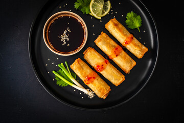 Vegetable filled spring rolls and soy sauce on black wooden table
