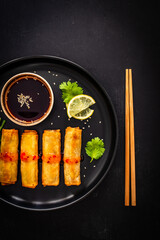 Vegetable filled spring rolls and soy sauce on black wooden table
