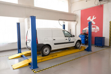 White van on a lift in a workshop, ready for servicing. Auto repair shop with a car on a lifting platform. Car in auto repair shop mechanical car repair at service station.