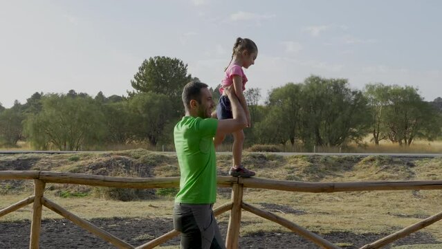 Father Teaching Daughter on Countryside Fence - Dad carefully guides his daughter on a fence walk, setting the stage for an endearing family scene.