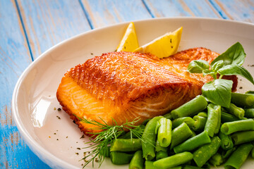 Seared salmon steak with green bean and lemons on wooden table
