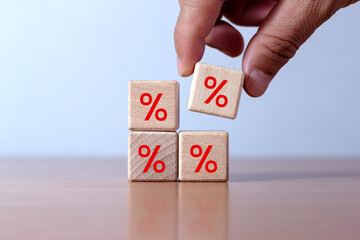Financial interest rate and mortgage rate concept, hand placed wooden block rising above with percent symbol icon, upward direction.