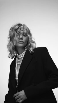 A beautiful woman with loose hair, in a jacket and beads, poses in the studio in a black and white video