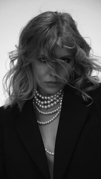 A beautiful woman with loose hair, in a jacket and beads, poses in the studio in a black and white video