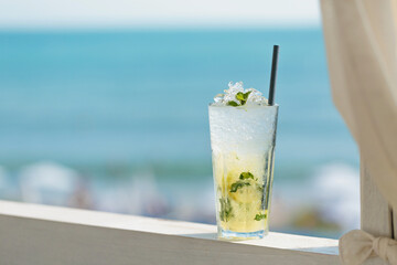 Glass of majito cocktail on terrace against blue sea. Cool drink on hot sunny day in cafe by the sea