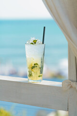 Glass of majito cocktail on terrace against blue sea. Cool drink on hot sunny day in cafe by the sea