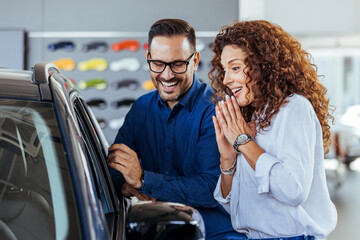 Happy couple buying car in auto show or salon. It is the one car I want! Beautiful young couple standing at the dealership choosing the car to buy. Couple at car showroom choosing a new car to buy.