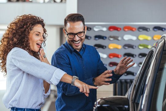 Happy couple buying car in auto show or salon. It is the one car I want! Beautiful young couple standing at the dealership choosing the car to buy. Couple at car showroom choosing a new car to buy.