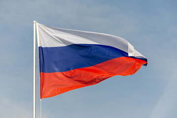 Naklejka premium Russian flag flag of flies against a clear blue sky with white clouds. Close-up, perfect for news