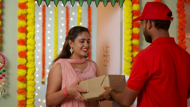 Happy excited girl receiving delivery box from delivery boy by signing on papers during Diwali festival day - concept of festive ecommerce order, fast delivery service and online shopping.