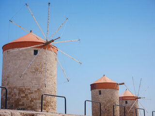 Windmills in the Mandraki port of Rhodes, Greece. Old defensive stands and windmills. Wharf harbors, boats and sailing ships. Historic pier and beach. Travel to Mediterranean islands Rhodes.