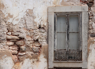 Old white damaged stone wall with ruined plaster and vintage window (Algarve, Portugal)