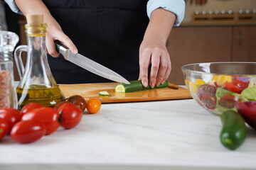 The woman in the process of making vegetable salad. Closeup of hands  cutting cucumber on wooden cutting board