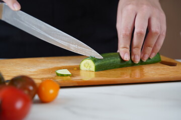 The woman in the process of making vegetable salad. Closeup of hands  cutting cucumber on wooden cutting board