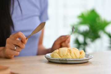 Pretty young asian woman eating pastry with great pleasure while spending weekend time at home