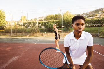 Close up of a young beautiful woman playing double tennis match on a sunny day. Young woman on tennis court holding a tennis racket focusing on the game.