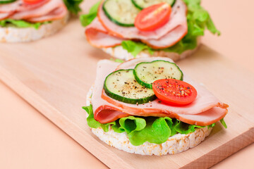 Light Breakfast. Quick and Healthy Sandwiches. Rice Cakes with Ham, Tomato, Fresh Cucumber and Green Salad on Wooden Cutting Board. Beige Background