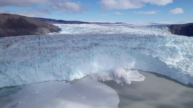 Aerial view of Eqi Glacier calving and creating tsunami waves by the breaking of ice chunks from the edge of a glacier. Elevated view of glacier collapsing on Arctic Ocean. Eqi Glacier, Greenland