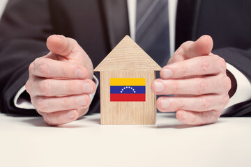 Businessman hand holding wooden home model with Venesuela flag. insurance and property concepts