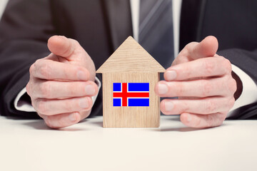 Businessman hand holding wooden home model with Icelandic flag. insurance and property concepts