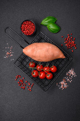 Fresh large pink sweet potato tubers with tomatoes and spices on a dark background